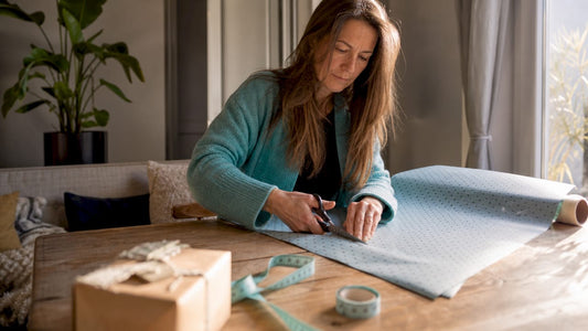 Aan de keukentafel is een vrouw bezig om een stuk standaard cadeaupapier op maat te knippen.